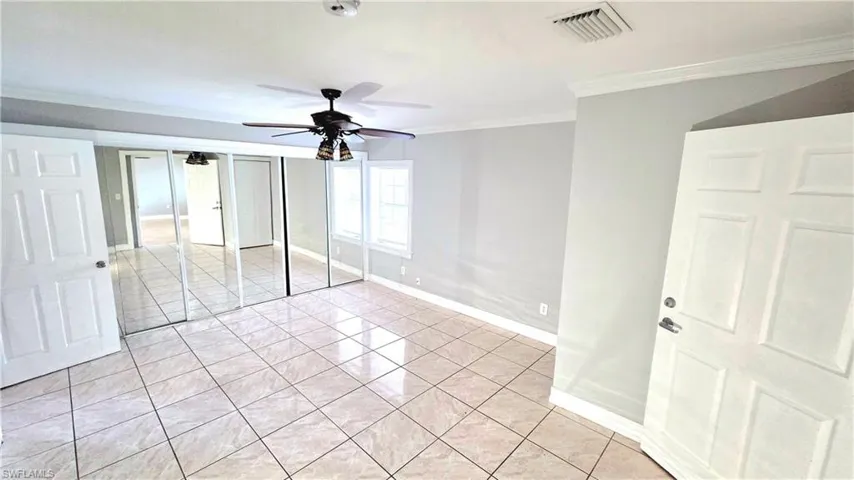 Spacious room featuring light-colored tile flooring, full-wall mirrored closet doors, a ceiling fan with integrated lighting, and two windows providing natural light