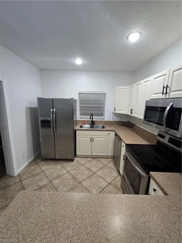 Kitchen with refrigerator, stove, white cabinets, a sink, and dishwashing machine