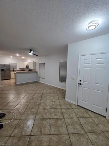 Unfurnished living room with tile patterned flooring, ceiling fan, a textured ceiling, and baseboards