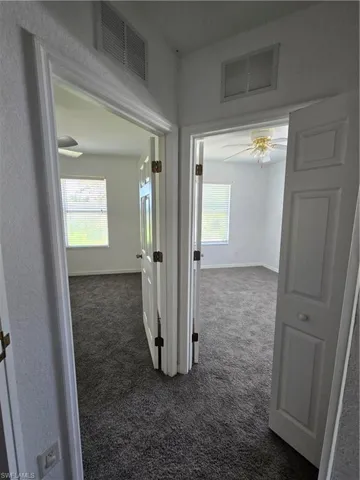 Hallway featuring dark colored carpet, visible vents, and a healthy amount of sunlight
