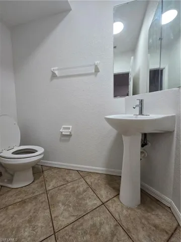 Bathroom with tile patterned flooring, baseboards, a textured wall, and toilet