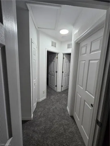 Corridor featuring a textured wall, dark colored carpet, visible vents, and baseboards