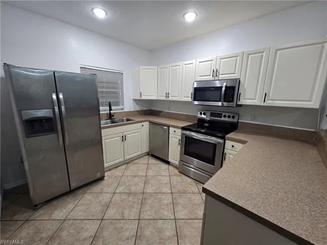 Kitchen featuring light tile patterned floors, recessed lighting, a sink, white cabinetry, and appliances with stainless steel finishes