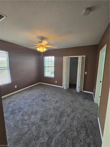 Unfurnished bedroom featuring visible vents, baseboards, dark colored carpet, and a textured ceiling