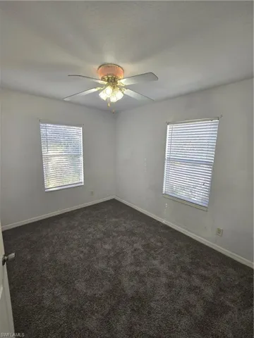Unfurnished room with dark colored carpet, plenty of natural light, and baseboards