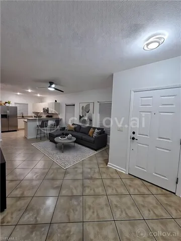 Unfurnished living room featuring light tile patterned flooring, a ceiling fan, and a textured ceiling