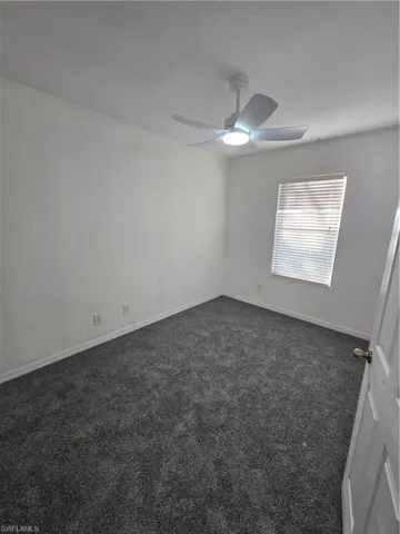 Spare room with baseboards, dark carpet, and ceiling fan