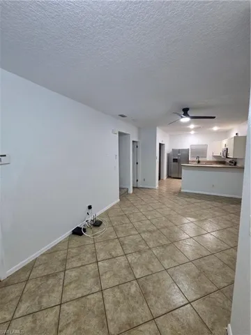 Unfurnished living room featuring a textured ceiling, baseboards, a ceiling fan, and light tile patterned flooring