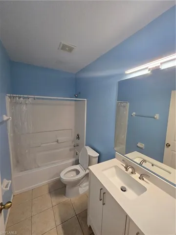 Full bathroom featuring a textured ceiling, toilet, visible vents, tile patterned floors, and shower / bath combination with curtain