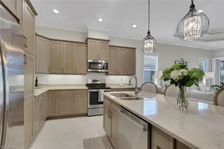 Kitchen with stainless steel appliances, light stone countertops, suspended lighting, and wood finish cabinetry