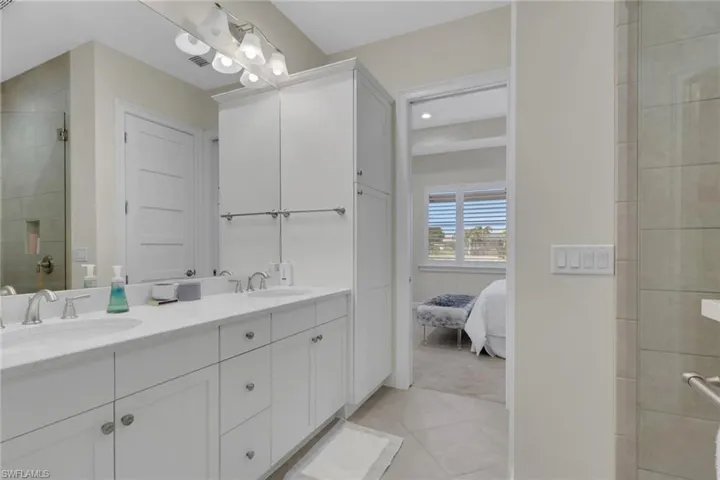 Ensuite bathroom with double vanity, light tile patterned flooring, tiled shower, and recessed lighting