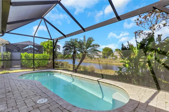 Swimming pool with glass enclosure, a sunroom, a water view, and a patio