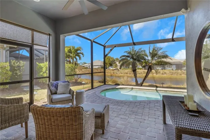 Outdoor pool with glass enclosure, a sunroom, a water view, and a patio area