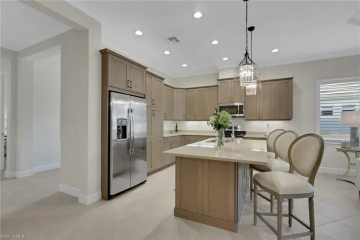 Kitchen with stainless steel appliances, a kitchen breakfast bar, a center island, light stone countertops, and suspended lighting