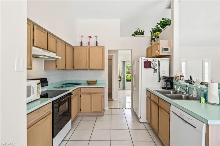 Kitchen featuring white appliances, backsplash, sink, light tile floors, and light brown cabinets