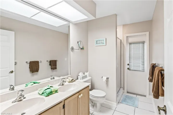 Bathroom featuring a shower with door, tile flooring, toilet, and dual bowl vanity