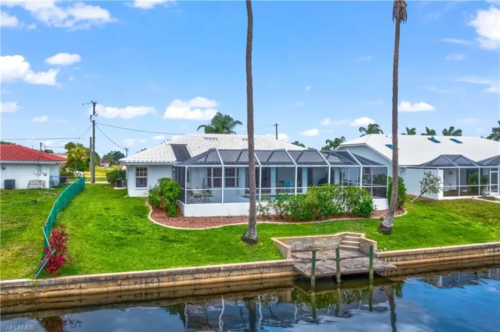 Rear view of property with glass enclosure, a water view, and a yard