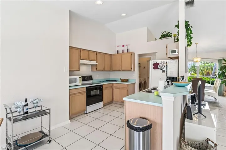 Kitchen featuring washing machine and clothes dryer, white appliances, backsplash, high vaulted ceiling, and light tile floors