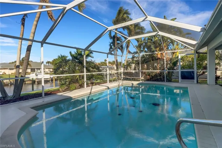 View of pool with glass enclosure, a patio area, and a water view