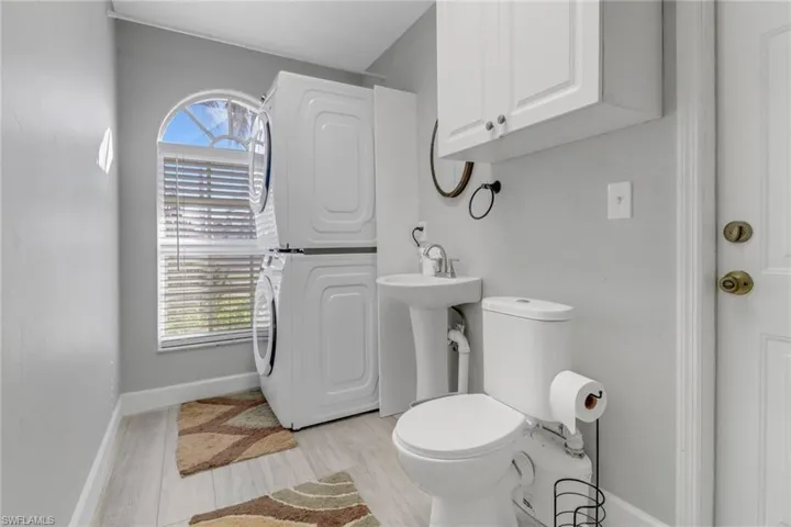 Bathroom featuring sink, wood-type flooring, stacked washer and clothes dryer, and toilet