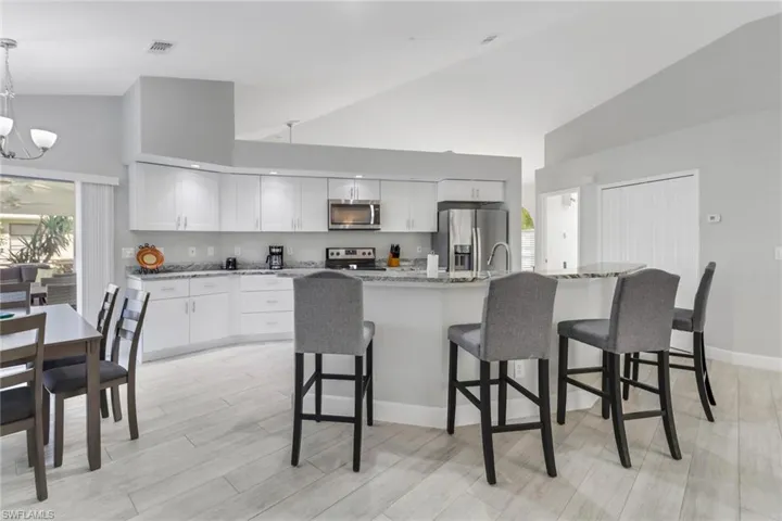Kitchen with high vaulted ceiling, white cabinets, decorative light fixtures, light stone counters, and stainless steel appliances