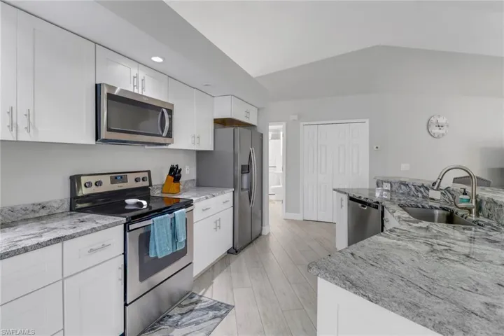 Kitchen with light stone countertops, white cabinetry, sink, light hardwood / wood-style floors, and appliances with stainless steel finishes