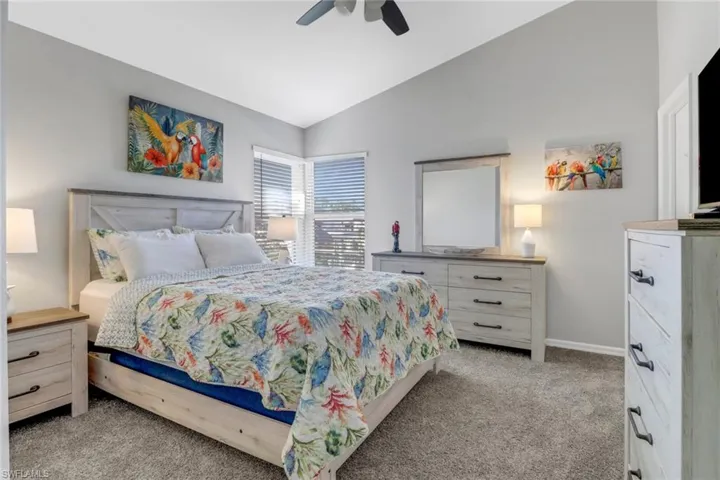 Bedroom with ceiling fan, light carpet, and vaulted ceiling