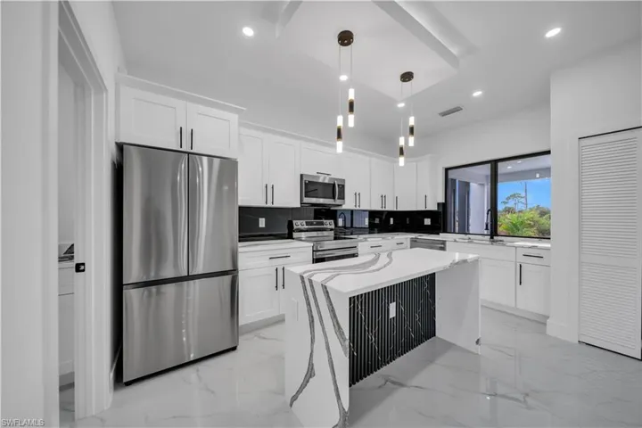 Kitchen with stainless steel appliances, light marble finish floors, white cabinetry, decorative light fixtures, and recessed lighting