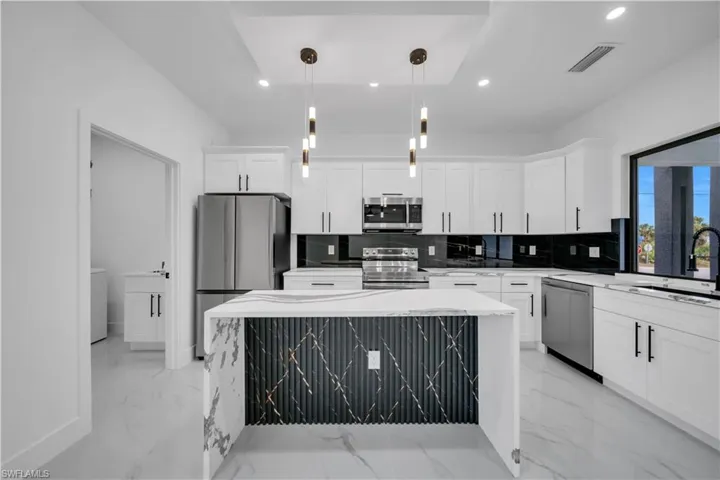 Kitchen with a center island, appliances with stainless steel finishes, light stone countertops, recessed lighting, and hanging light fixtures