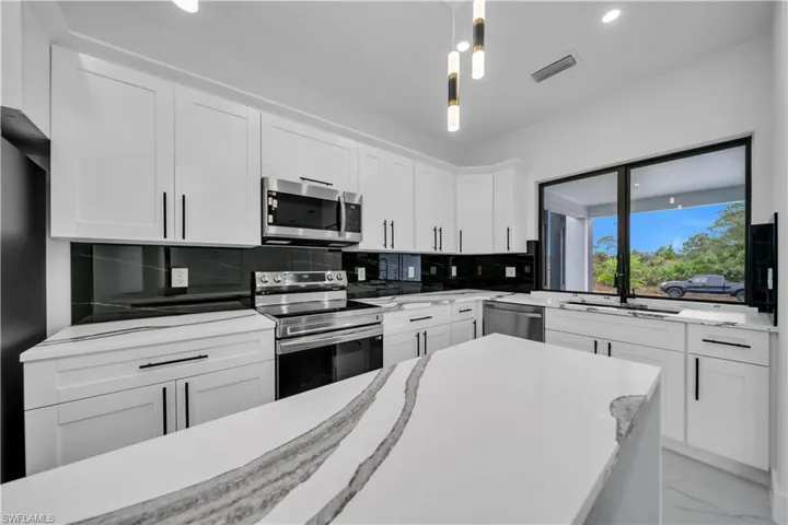 Kitchen with appliances with stainless steel finishes, white cabinetry, pendant lighting, light stone counters, and recessed lighting