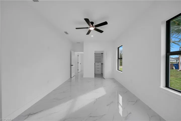 Unfurnished bedroom featuring a spacious closet, a ceiling fan, light marble finish floors, and recessed lighting