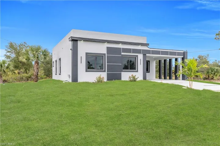 Contemporary house featuring a front yard, stucco siding, concrete driveway, and a carport