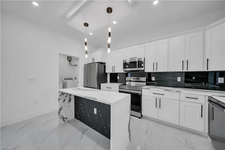 Kitchen featuring stainless steel appliances, decorative light fixtures, light marble finish flooring, white cabinets, and light stone counters
