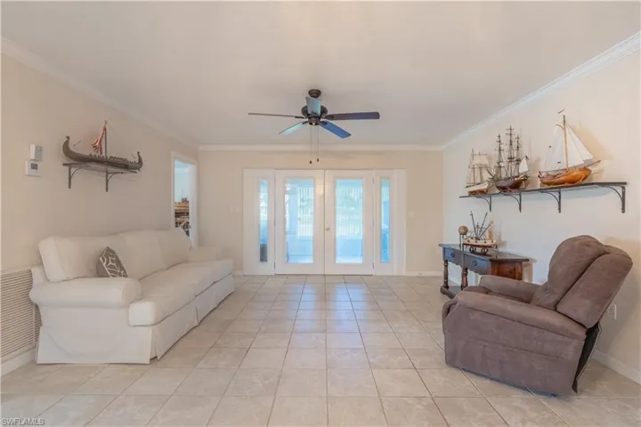Living room featuring ornamental molding, a ceiling fan, light tile patterned floors, and baseboards