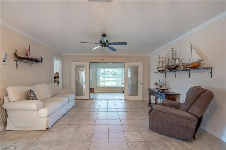 Living area with light tile patterned flooring, ceiling fan, ornamental molding, and baseboards