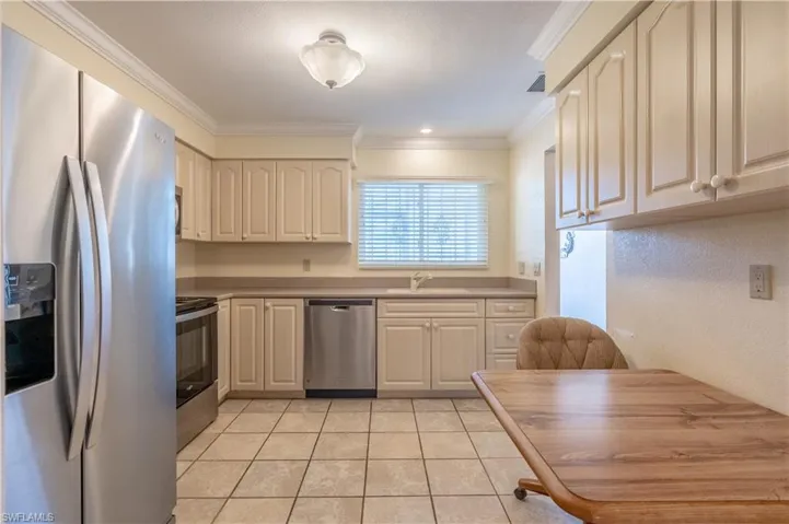 Kitchen with a sink, light tile patterned floors, light countertops, ornamental molding, and appliances with stainless steel finishes