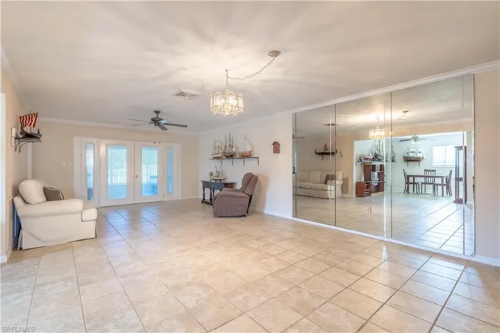 Living area featuring light tile patterned floors, ornamental molding, ceiling fan with notable chandelier, visible vents, and french doors