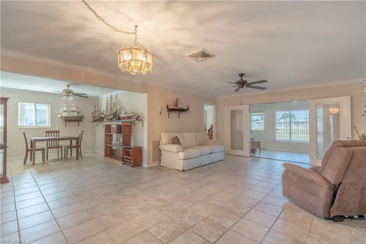 Living area featuring visible vents, crown molding, baseboards, and ceiling fan with notable chandelier