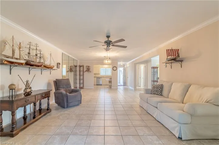 Living room with baseboards, light tile patterned floors, ceiling fan, and crown molding