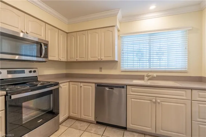 Kitchen with appliances with stainless steel finishes, light tile patterned flooring, crown molding, and a sink