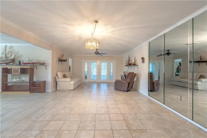 Tiled living area with french doors, crown molding, and ceiling fan with notable chandelier