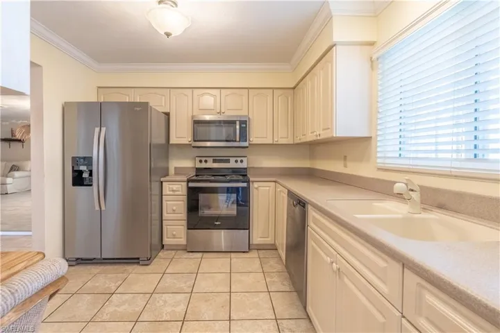 Kitchen featuring light tile patterned floors, a sink, appliances with stainless steel finishes, light countertops, and ornamental molding
