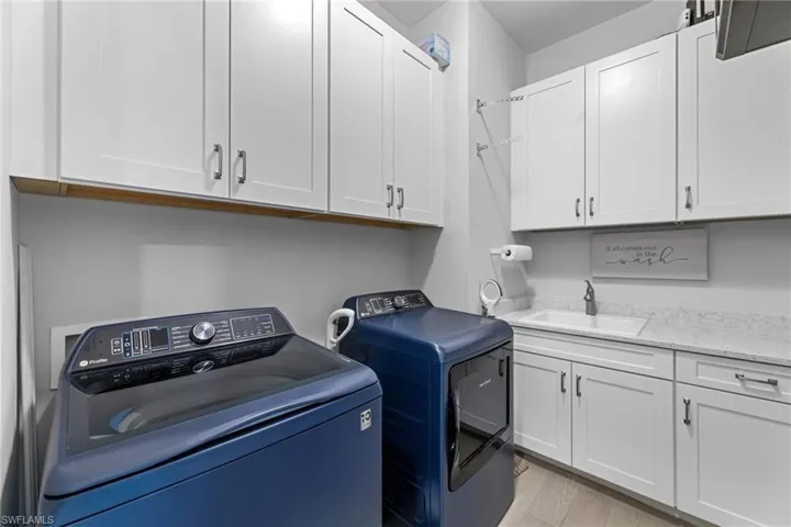 Laundry area featuring cabinets, separate washer and dryer, sink, and light hardwood / wood-style flooring