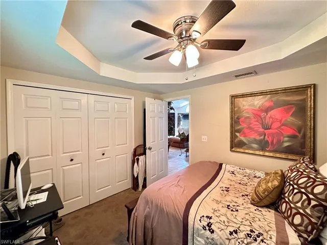 Bedroom with ceiling fan, dark carpet, a tray ceiling, and a closet