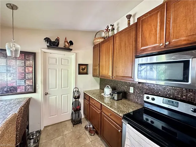 Kitchen featuring tasteful backsplash, appliances with stainless steel finishes, light tile patterned floors, hanging light fixtures, and vaulted ceiling