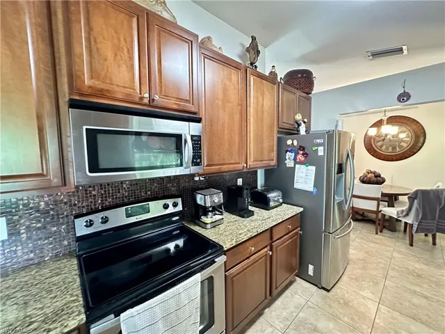 Kitchen featuring stainless steel appliances, light stone countertops, light tile patterned flooring, and tasteful backsplash