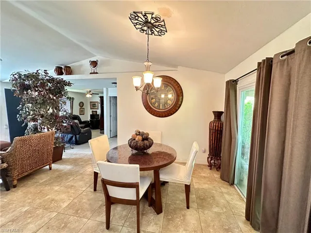 Dining area with ceiling fan with notable chandelier, lofted ceiling, and light tile patterned floors
