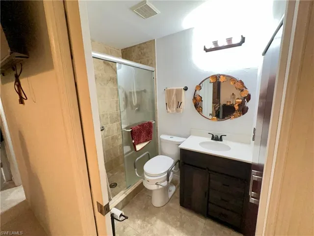 Bathroom featuring toilet, vanity, tile patterned flooring, and a shower with door