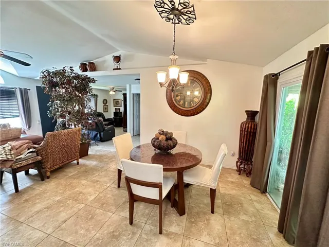 Dining space with a wealth of natural light, vaulted ceiling, and ceiling fan with notable chandelier