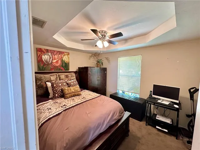 Carpeted bedroom featuring ceiling fan and a raised ceiling